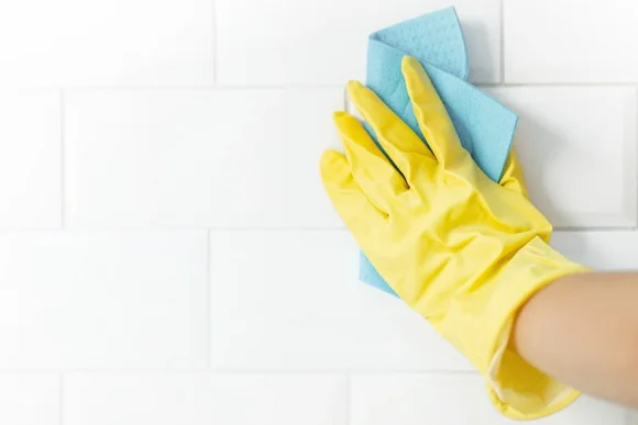 Hand in gelbem Gummihandschuh reinigt weiße Fliesen